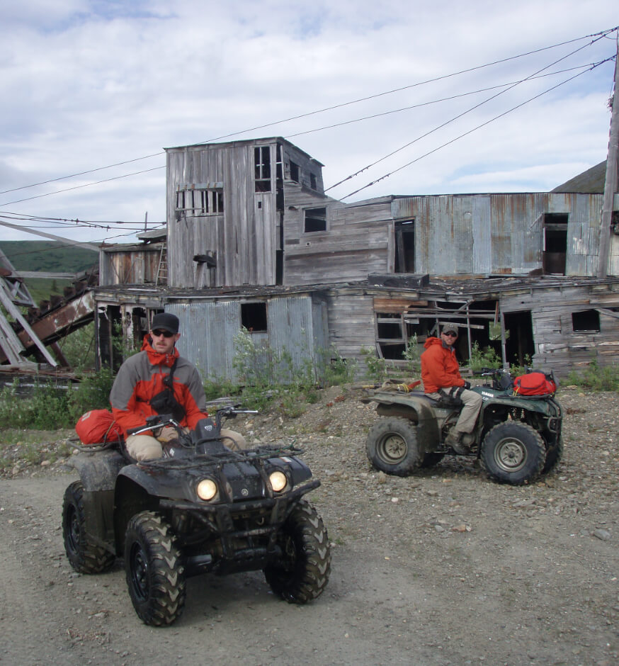 Two geologists on ATVs in front of an old Alaskan mine.