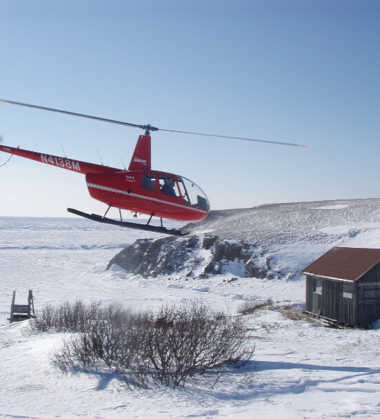 Helicopter comes in for a landing over a snowy field.