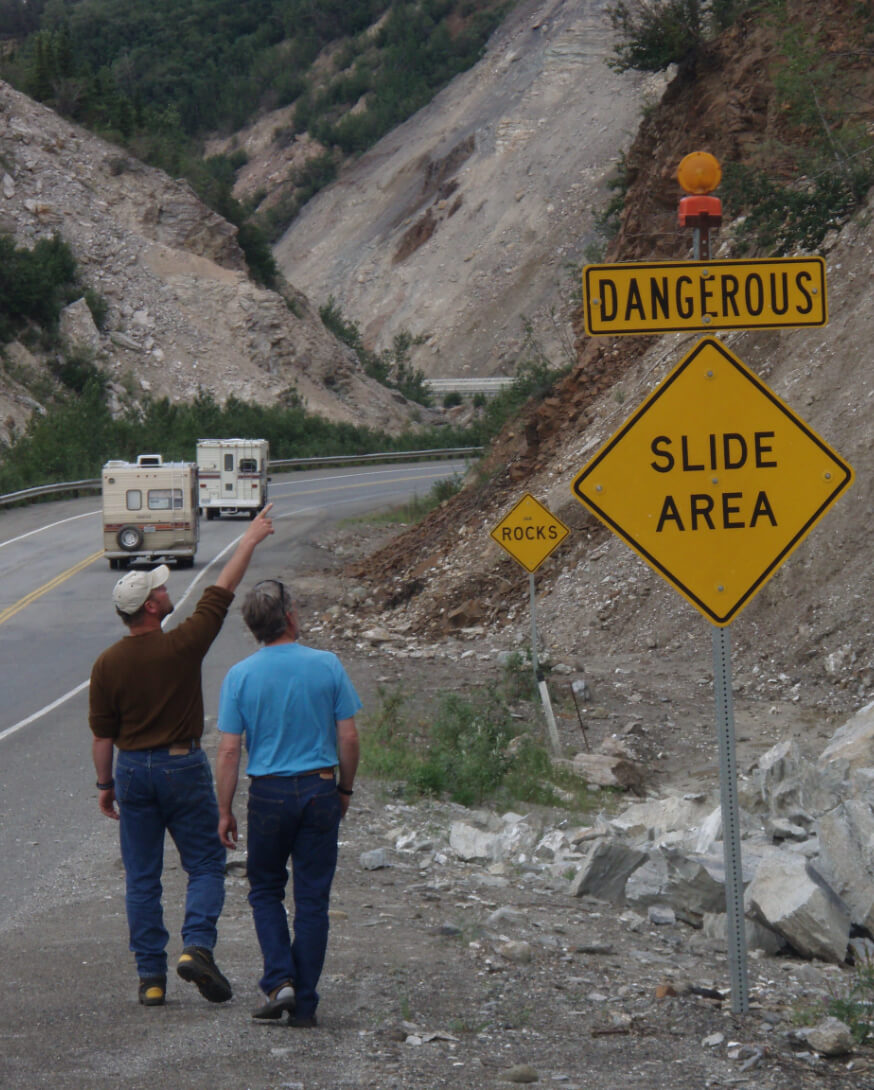 Two men look at a rock slide along the road.
