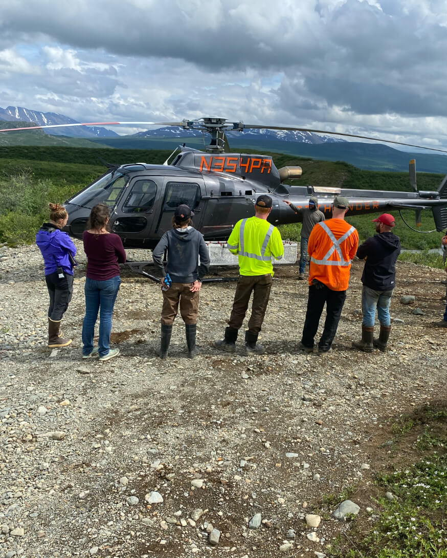 The crew next to a helicopter in the Alaskan wilderness.